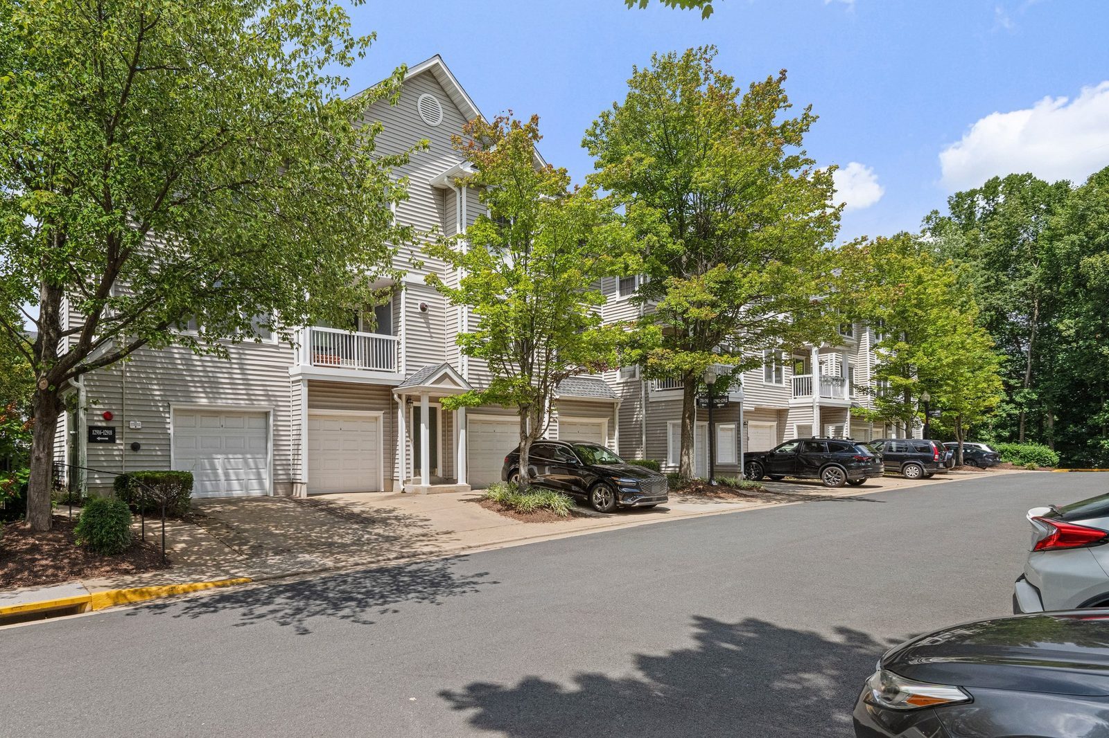 Row of garage doors and entries along a tree-lined community street