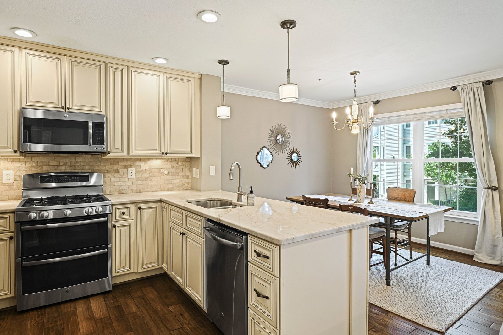 Kitchen with stone-look counters, cream cabinets, stainless range, open to dining area
