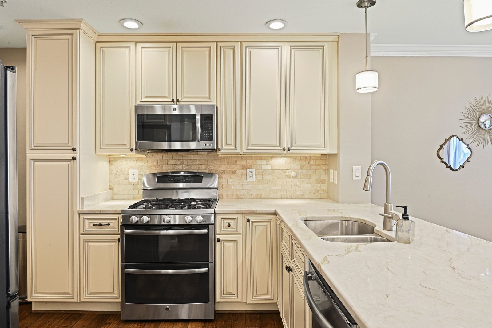 Cream cabinets, stainless gas range and microwave, tile backsplash, stone-look counters