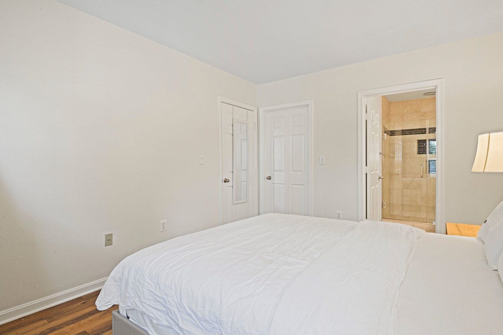 Bedroom corner with two white doors and doorway to tiled glass shower