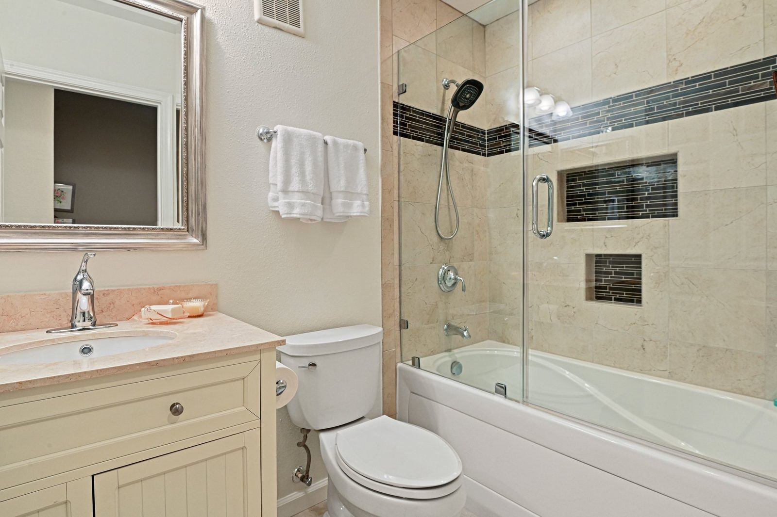 Full bathroom with glass-door tub shower, tiled surround and mosaic accent band