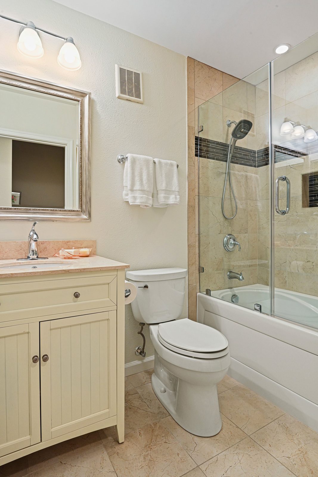 Bathroom vanity with stone counter, framed mirror and glass-enclosed tub shower