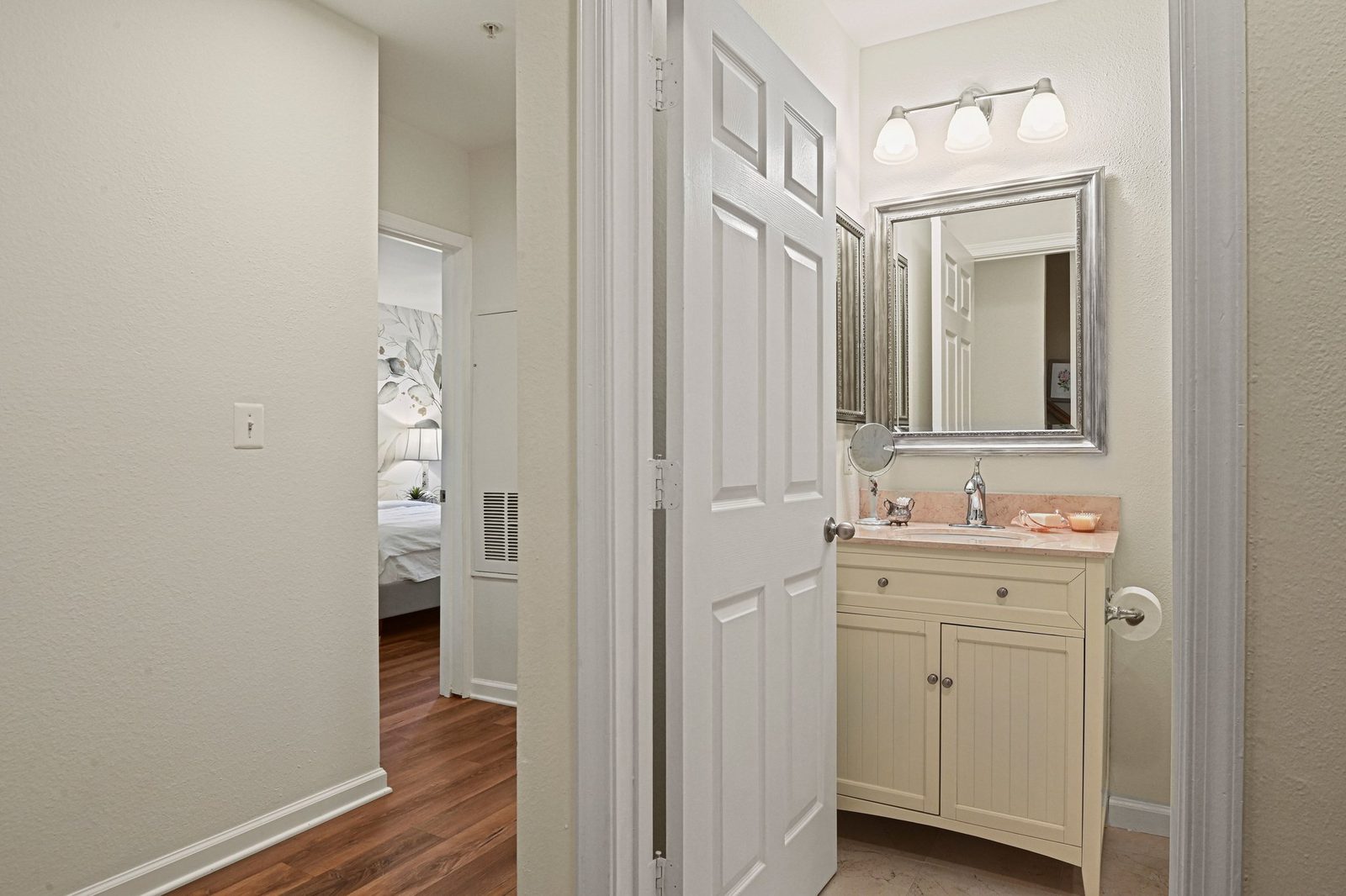 Hallway with vanity nook, framed mirror and doorway to a hardwood-floored bedroom
