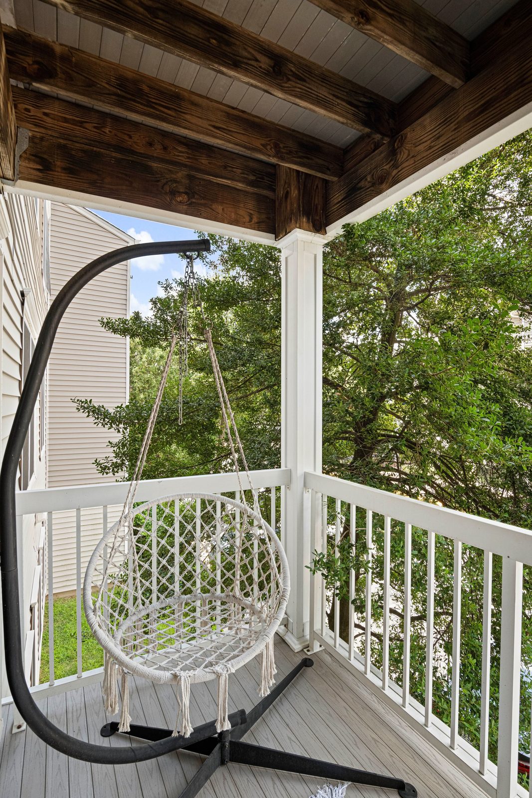 Covered balcony with hanging rope swing chair, white railing and exposed wood beams