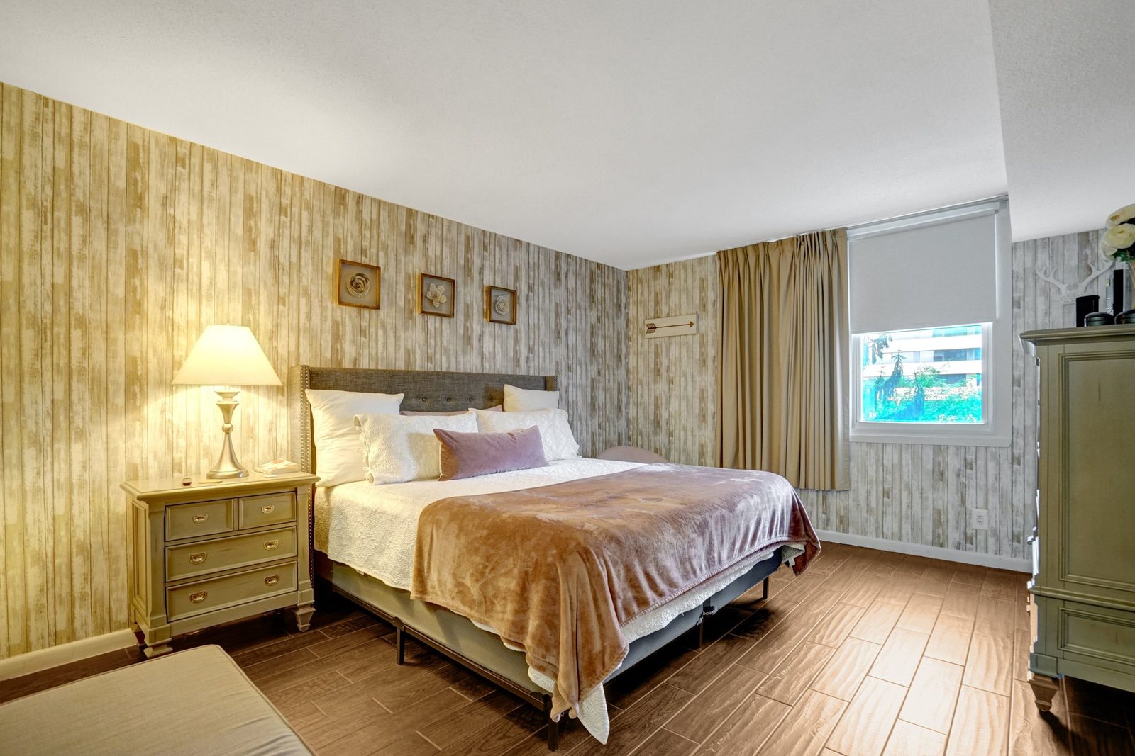 Bedroom with plank-pattern accent wall, curtained window and wood-look tile floor