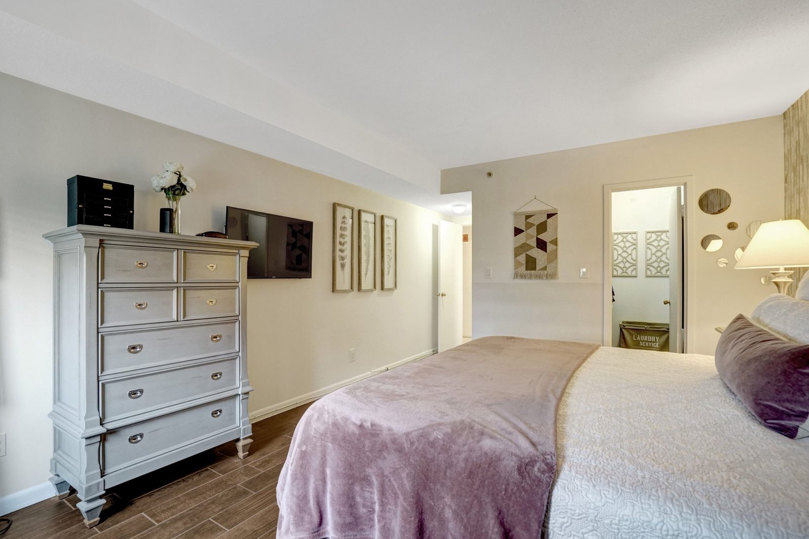Bedroom with tall dresser, mounted television and closet doorway