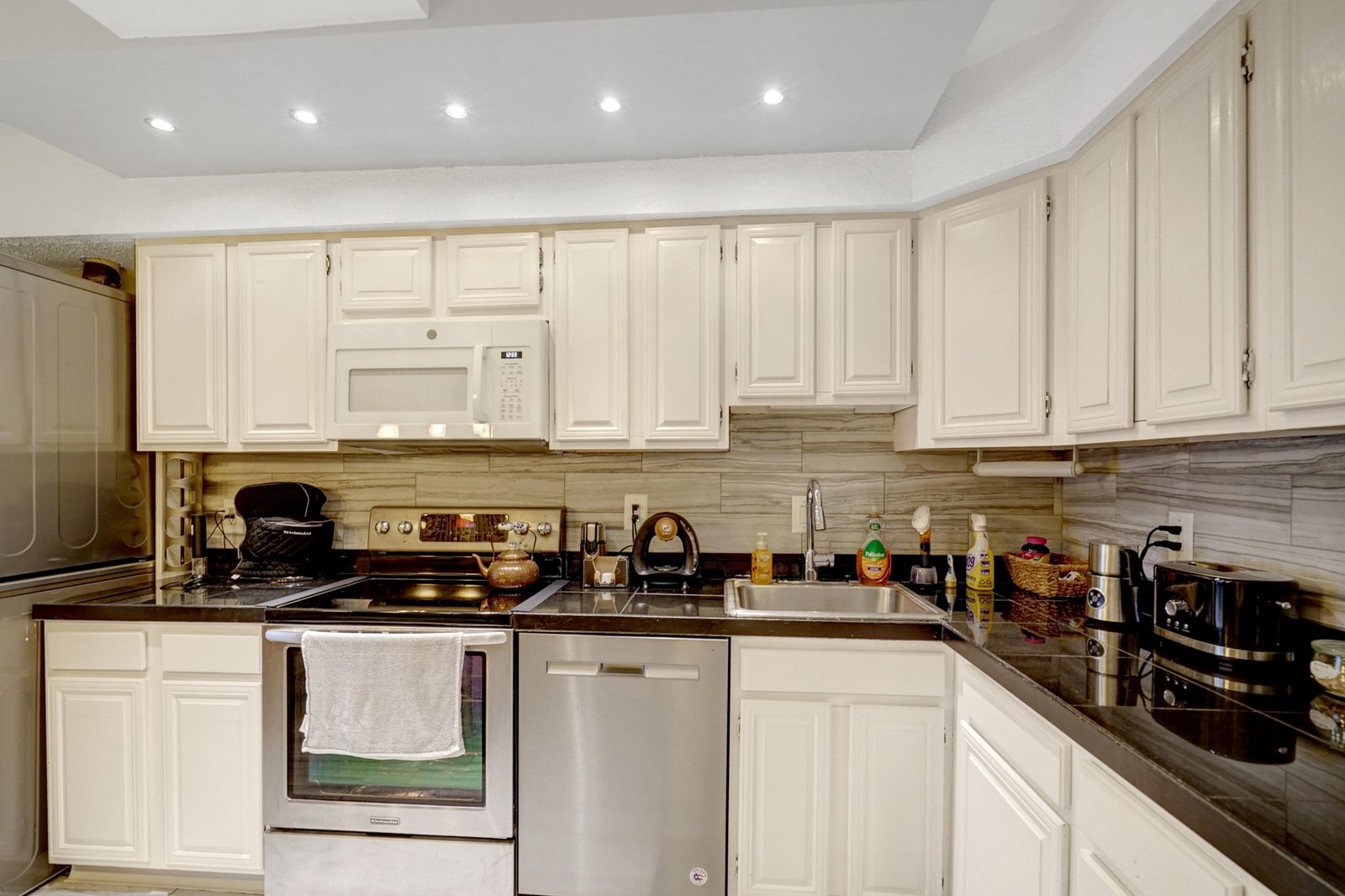 Kitchen with cream cabinets, dark counters and stainless dishwasher