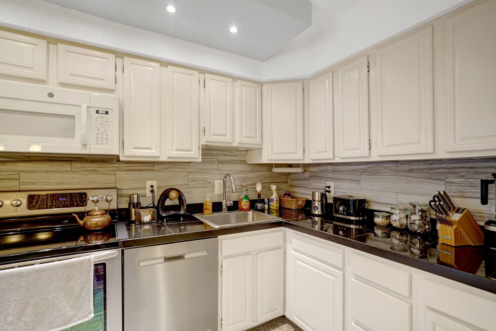 Kitchen corner with stainless sink, dark counters and white cabinets