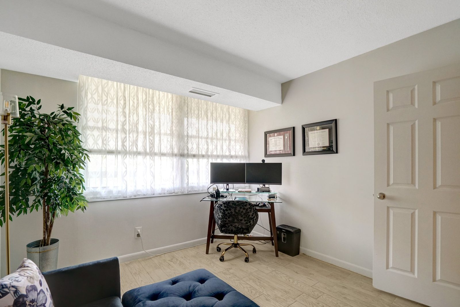 Room with wide window, plank flooring and glass-top desk