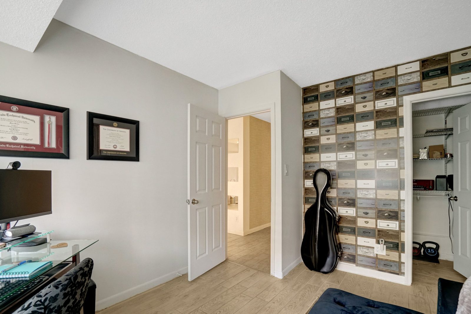 Room with patterned accent wall, open closet and plank flooring