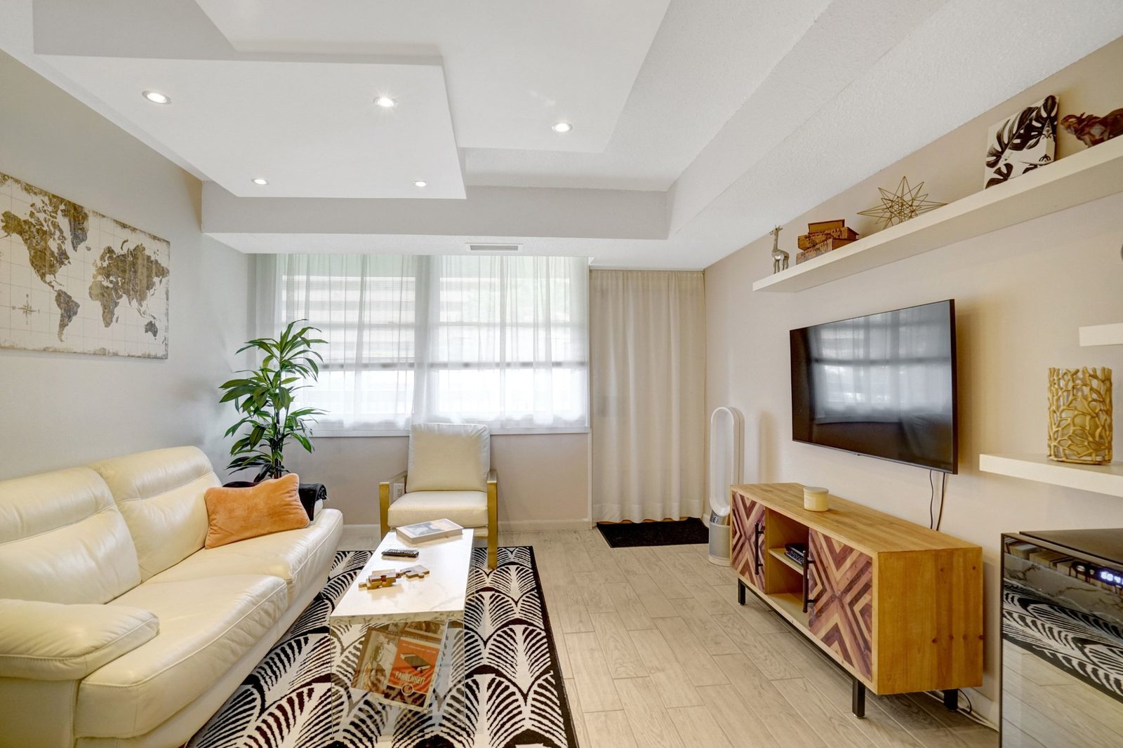 Living room with tray ceiling, wall-mounted TV and plank flooring