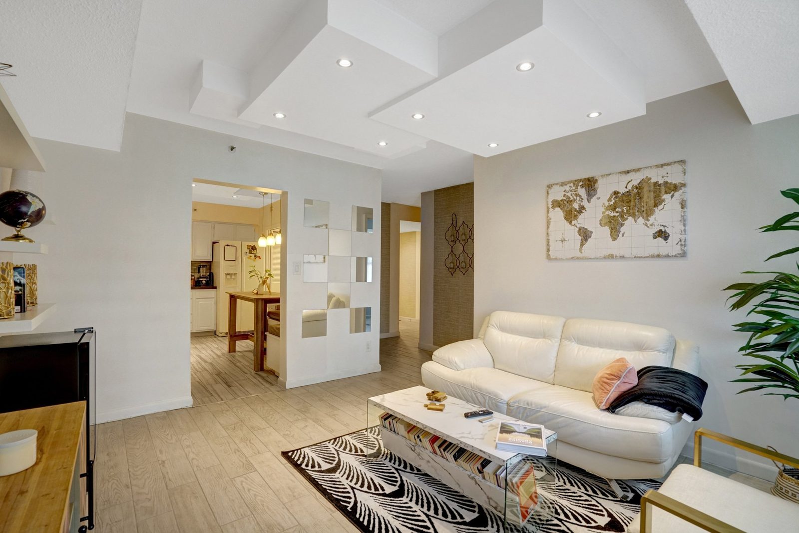 Living room opening to kitchen with mirrored accent panel and plank floors