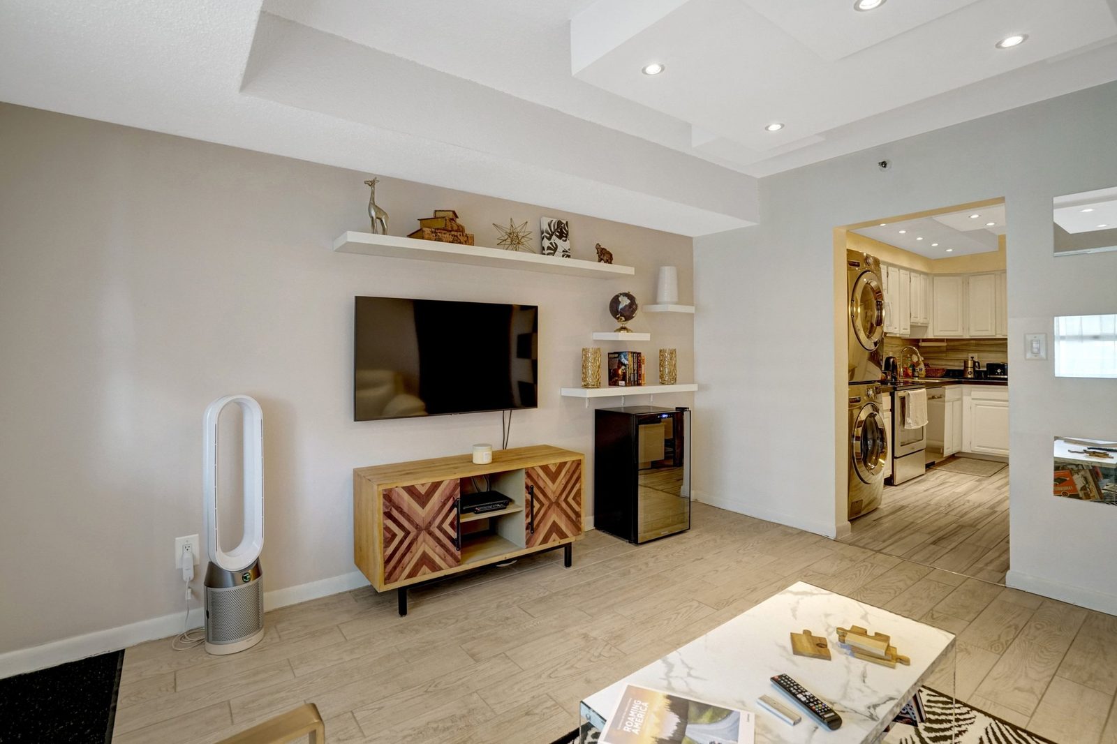 Living wall with mounted TV, floating shelves and view into kitchen
