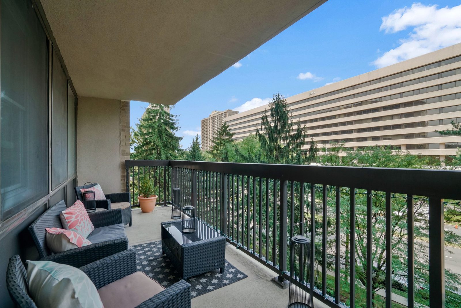 Covered balcony with wicker seating and treetop views of nearby buildings