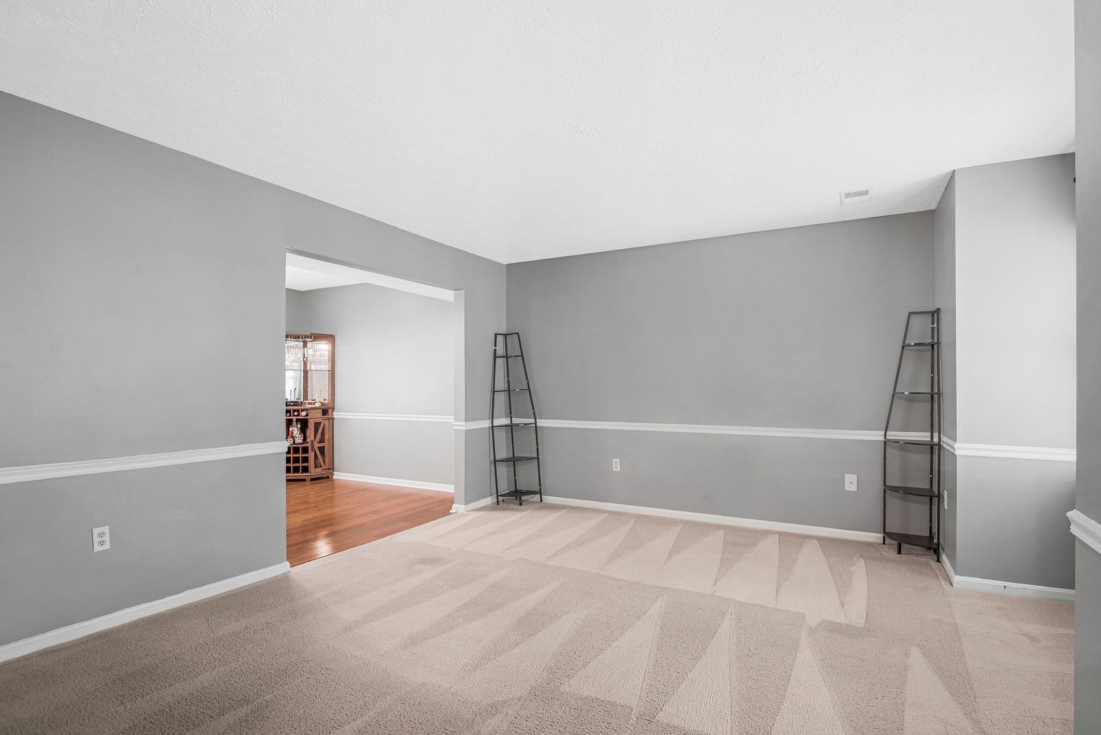 Empty carpeted living room with chair rail opening to wood-floor dining area