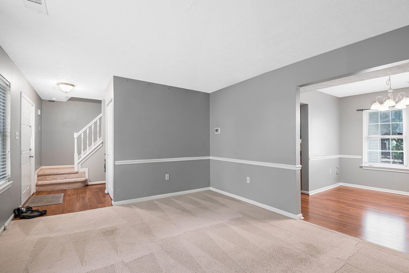 Carpeted living room with chair rail, staircase and dining room beyond