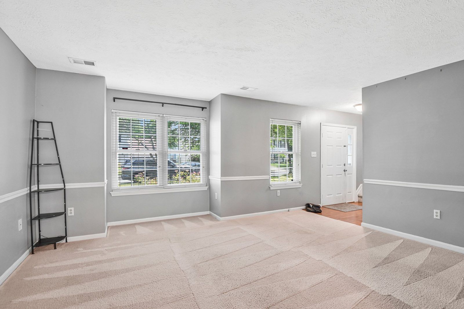 Bright carpeted living room with three blinded windows and front door