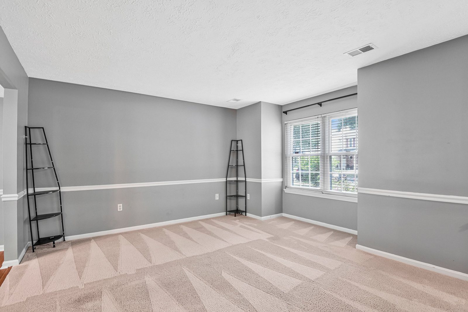 Carpeted room with chair rail, corner shelving and blinded window