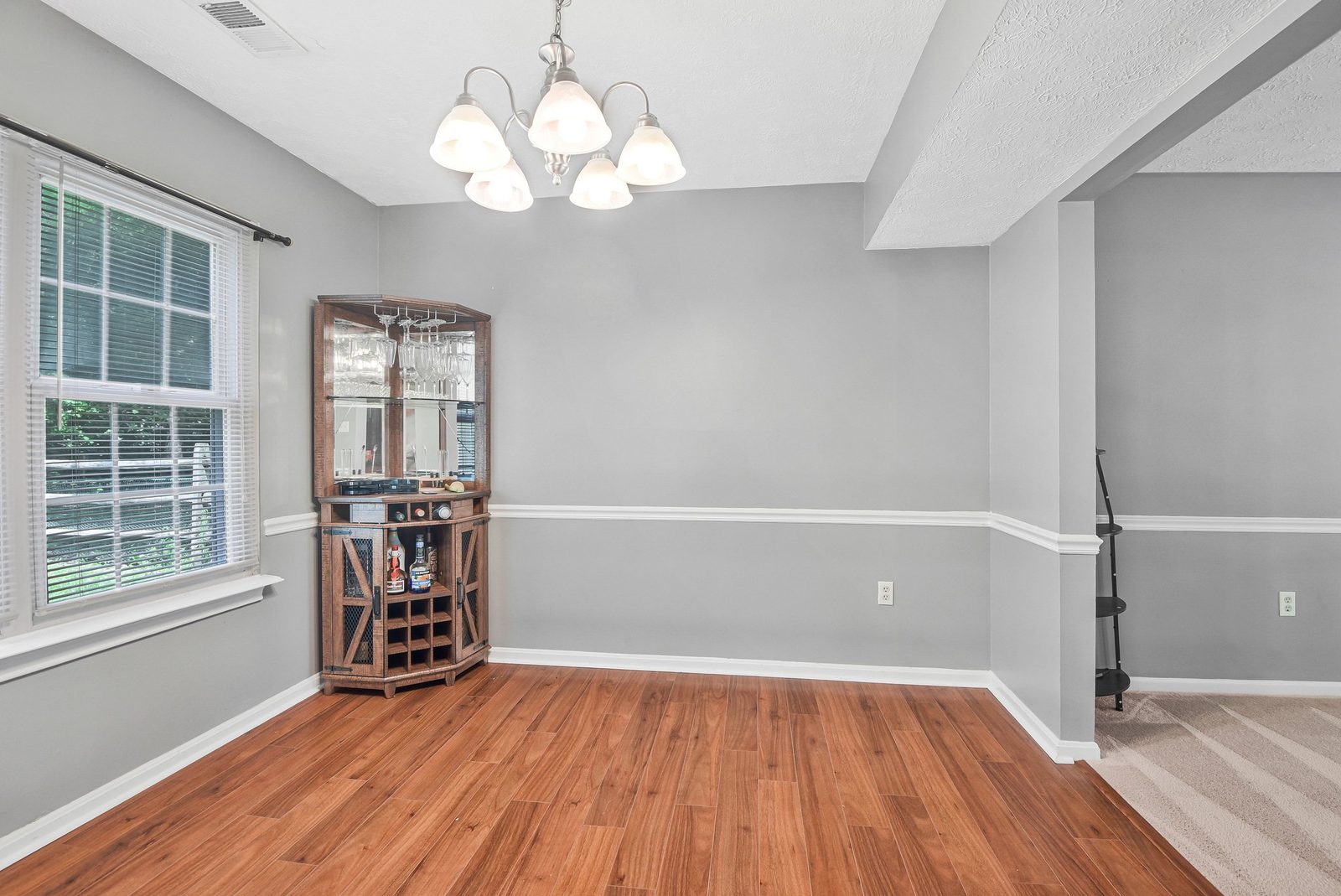 Wood-floor dining room with chandelier, window and corner wine cabinet