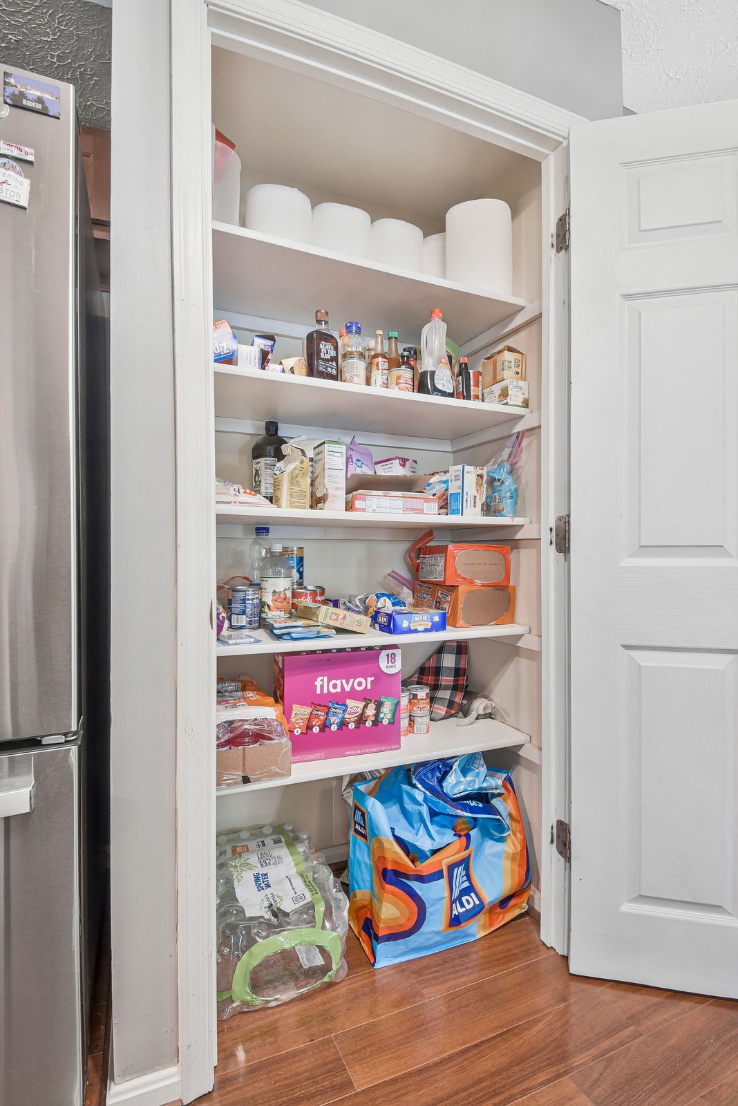 Open pantry closet with stocked shelves beside stainless refrigerator