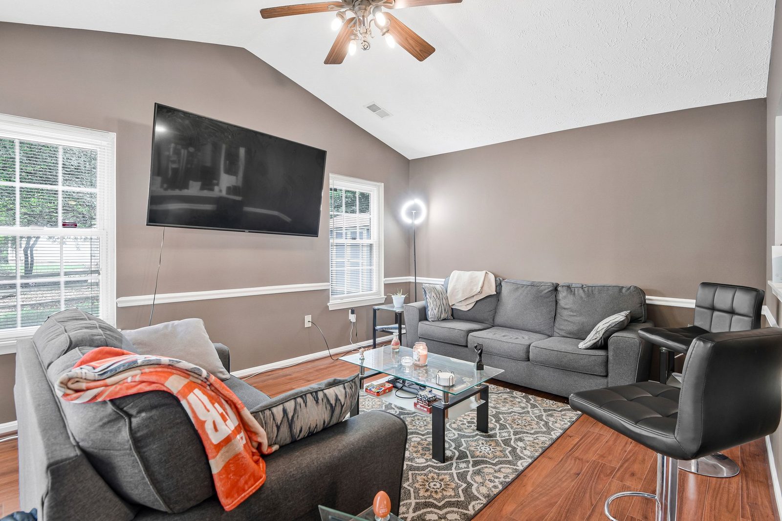 Vaulted living room with hardwood floors, ceiling fan and mounted TV