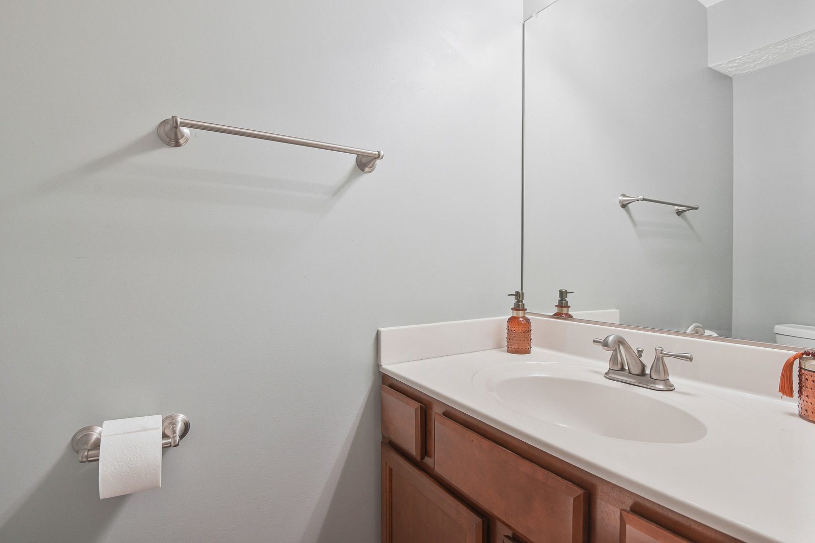 Bathroom vanity with white countertop, wood cabinets and full-width mirror