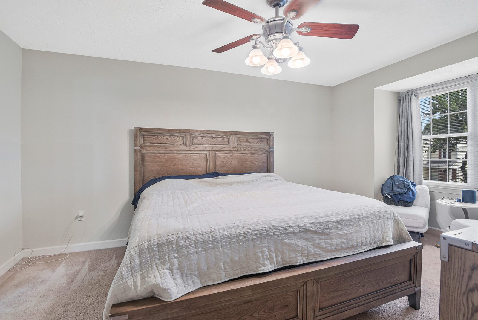 Carpeted bedroom with wood bed frame, ceiling fan and curtained window