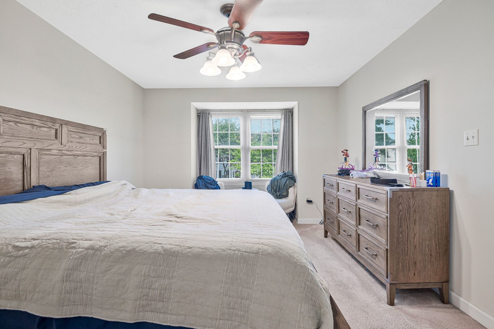 Carpeted bedroom with bay window, ceiling fan and wood dresser