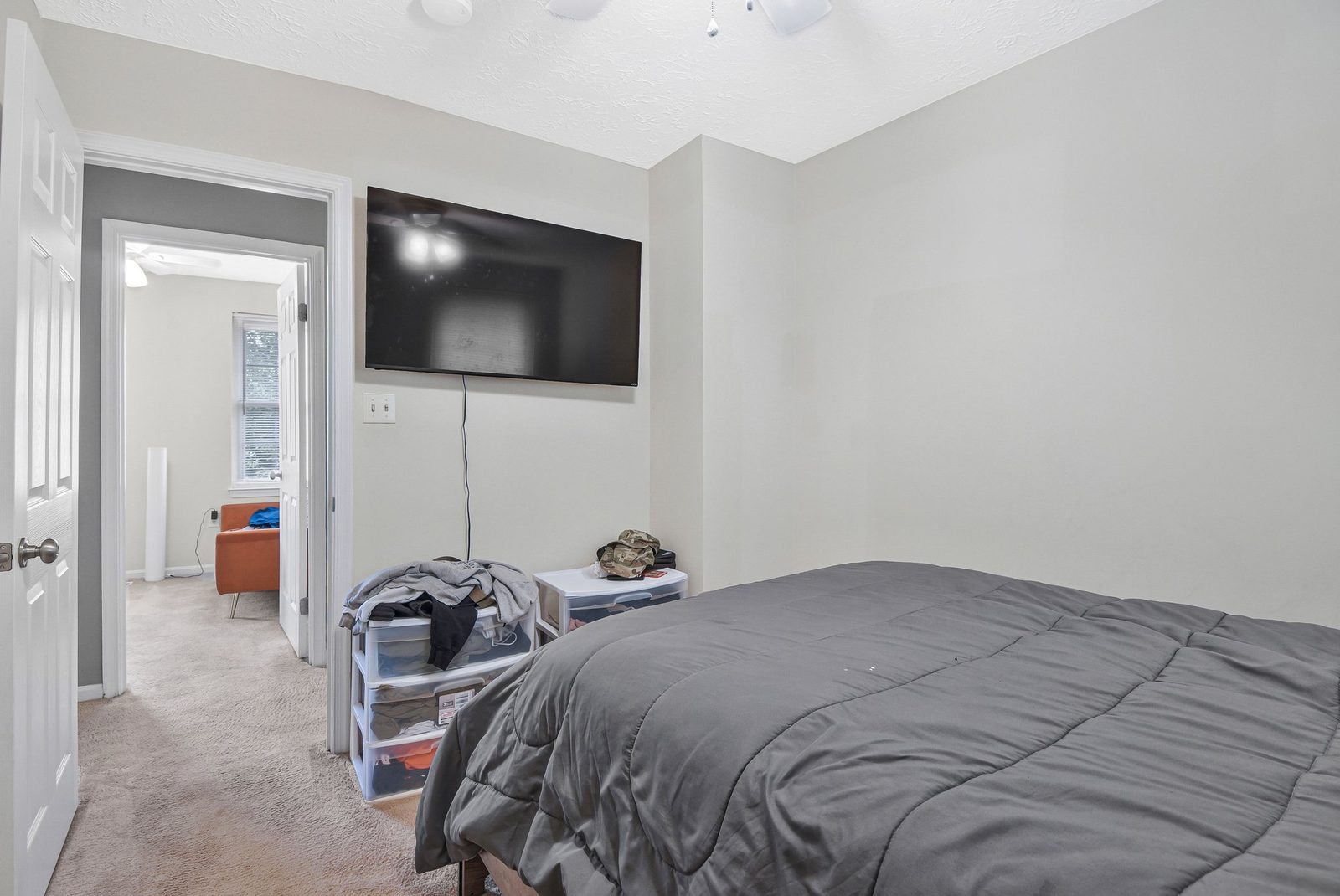 Carpeted bedroom with wall-mounted TV and doorway to adjoining room