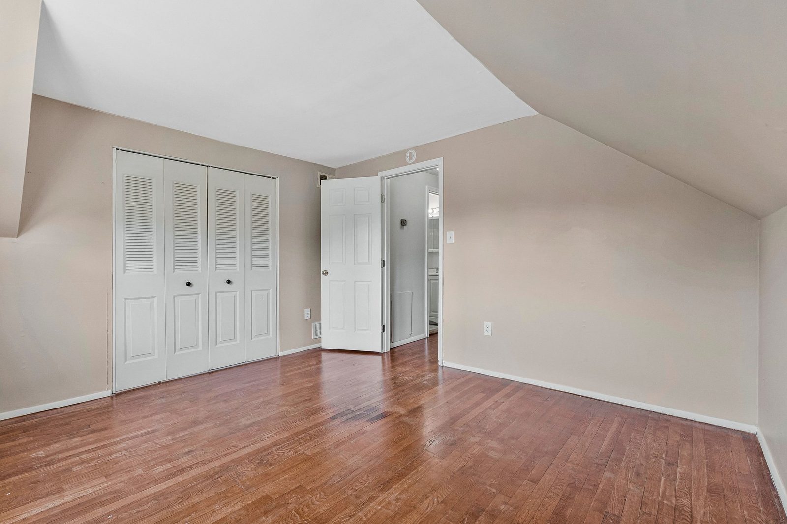 Sloped-ceiling room with louvered bifold closet doors and hardwood floors
