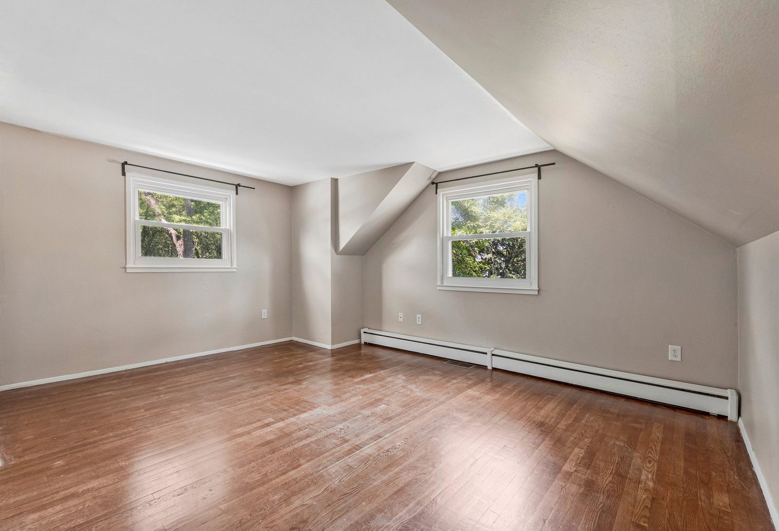 Sloped-ceiling room with two windows, hardwood floors and baseboard heat