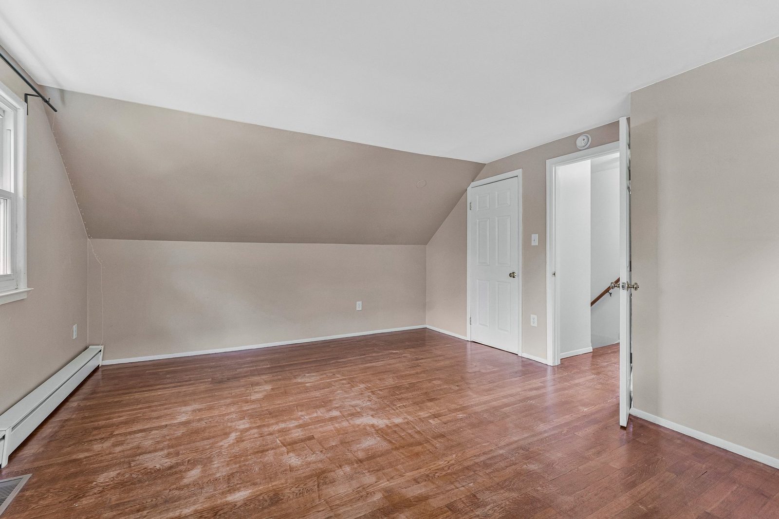 Sloped-ceiling room with hardwood floors, closet door and stair landing beyond