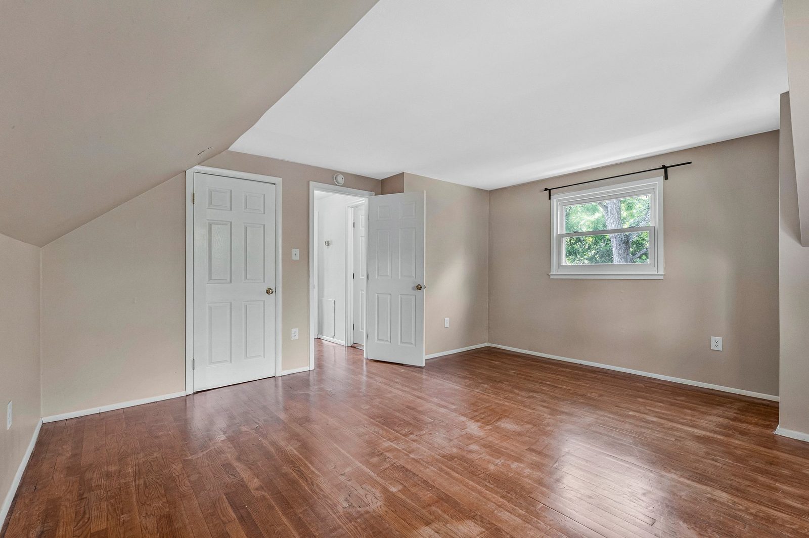 Upper-level room with two panel doors, window and hardwood floors