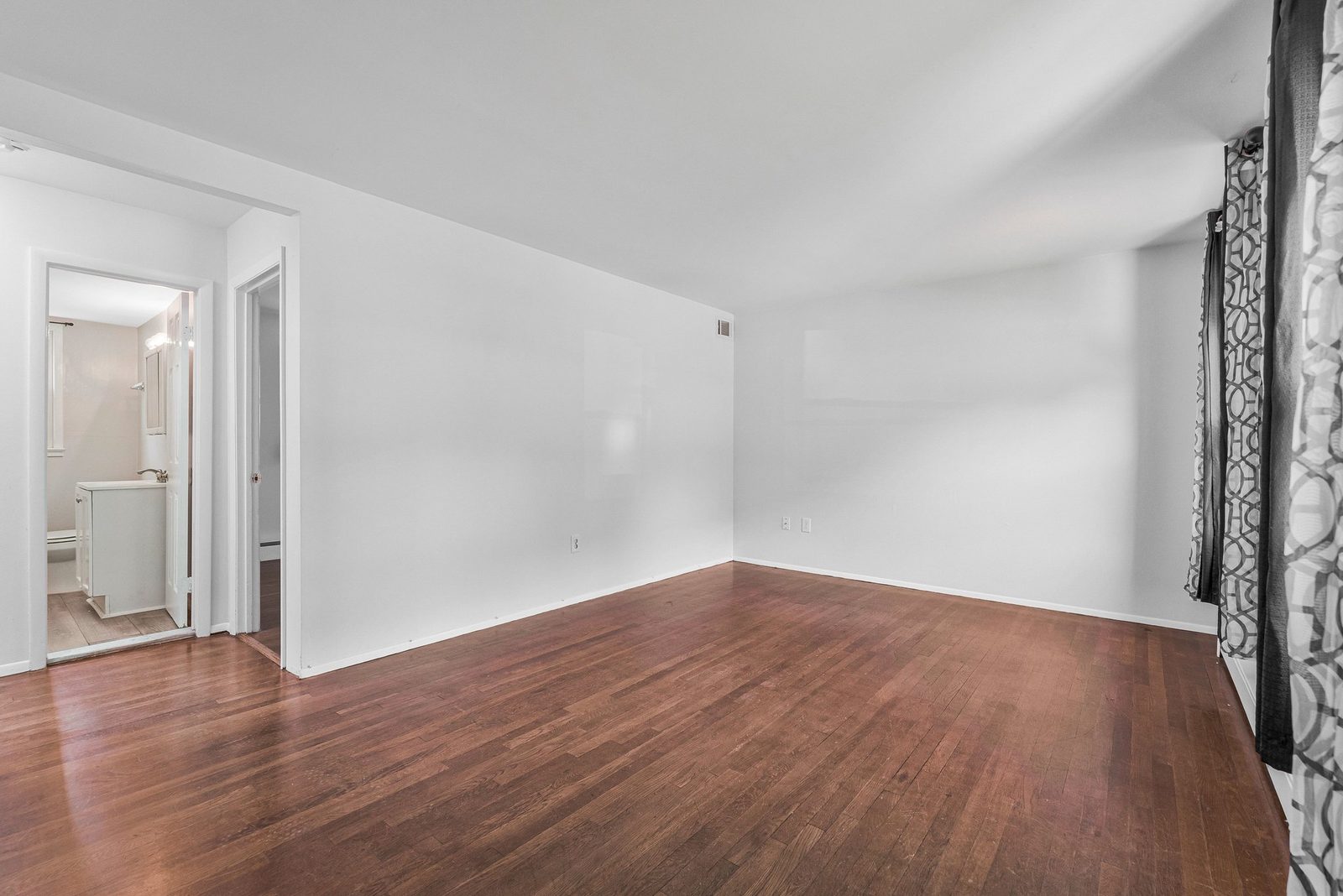 White-walled room with hardwood floors and doorway to adjoining bathroom