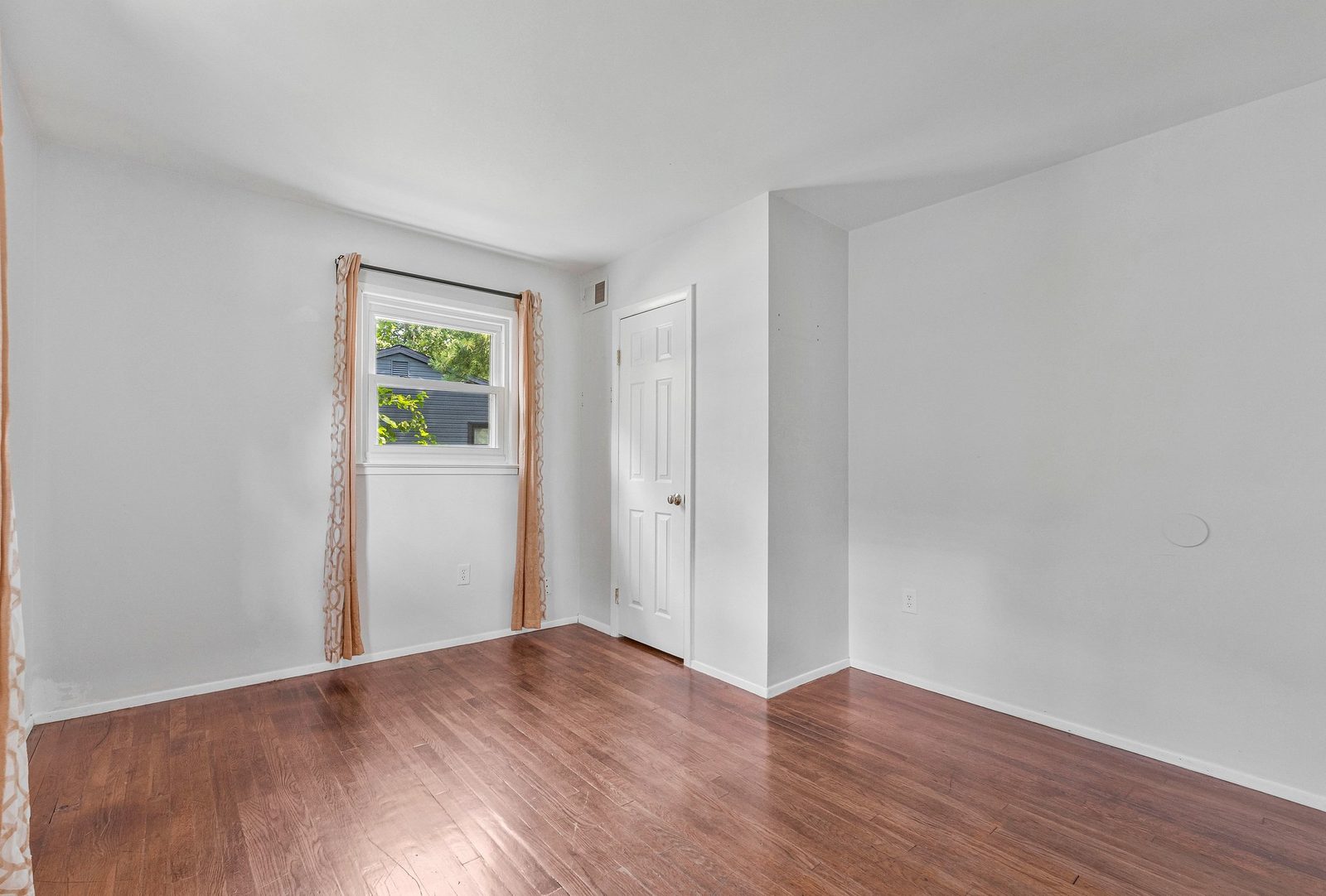 Room with hardwood floors, curtained window and white closet door