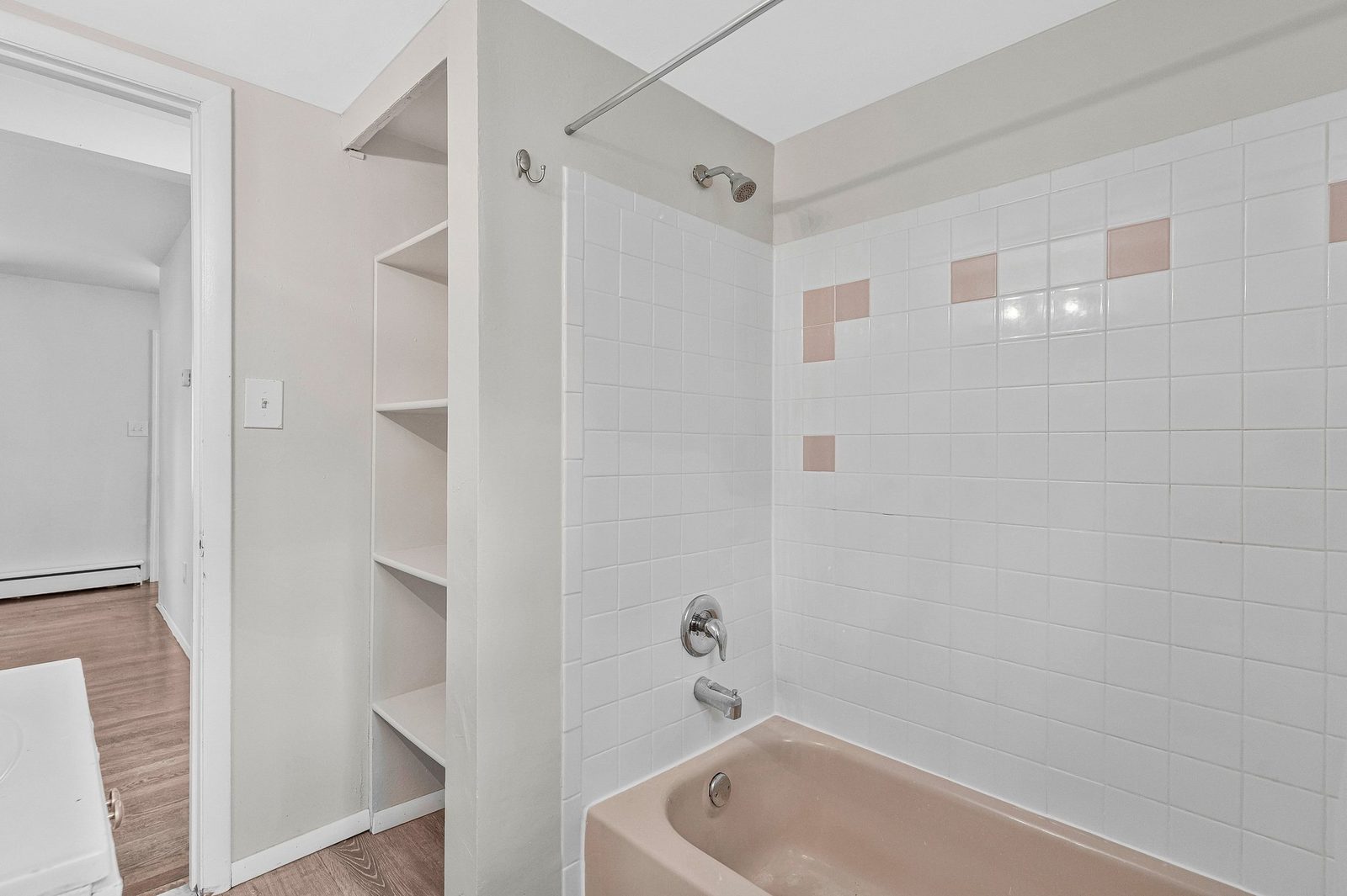Pink tub with white tile surround and built-in shelving alcove