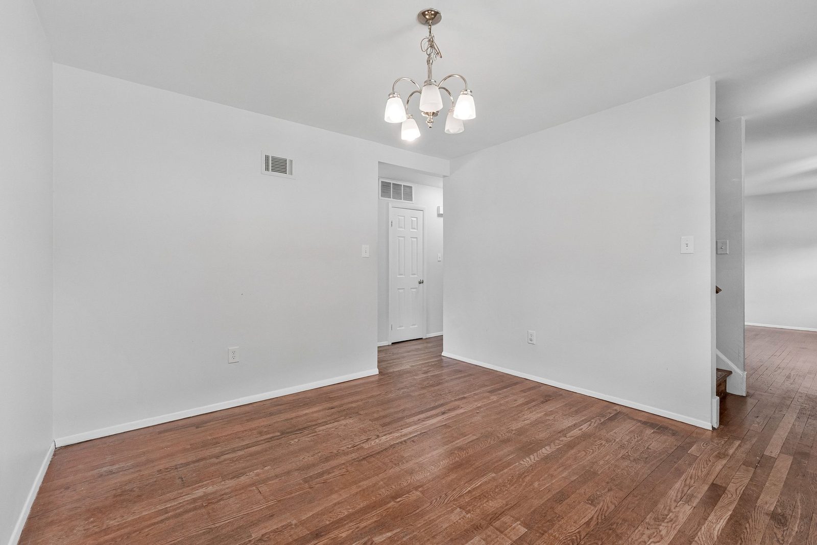 Empty room with chandelier, hardwood floors and stairs beyond