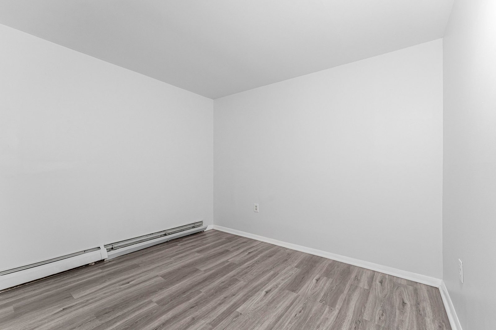 Empty corner with grey plank flooring and baseboard heater
