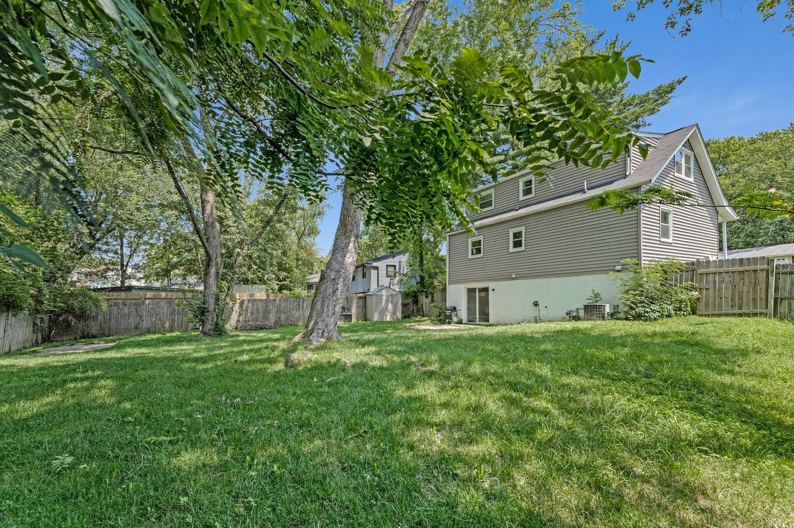 Side and rear view of grey-sided house from fenced yard