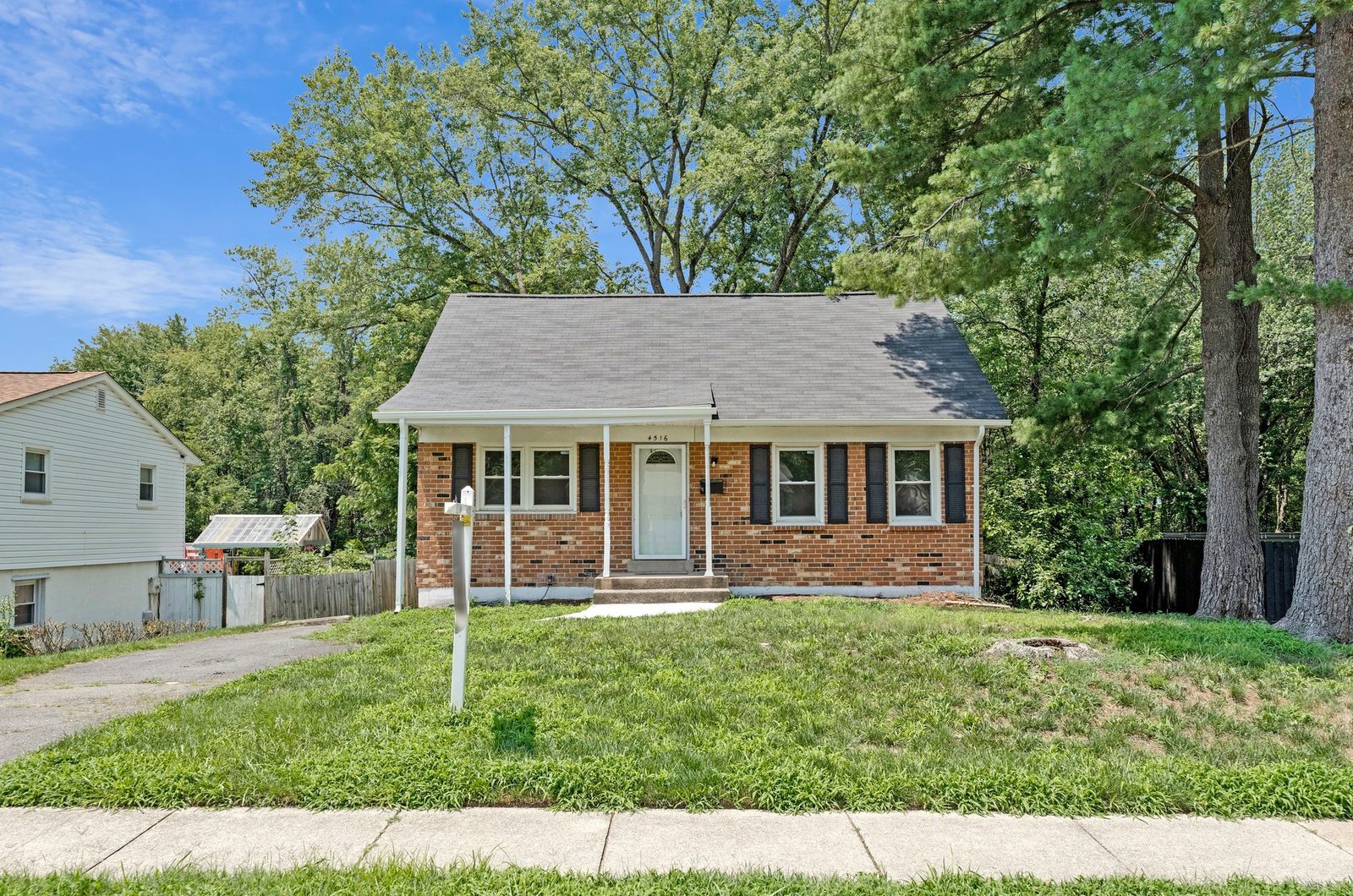Brick front exterior with covered porch, driveway and mature pines