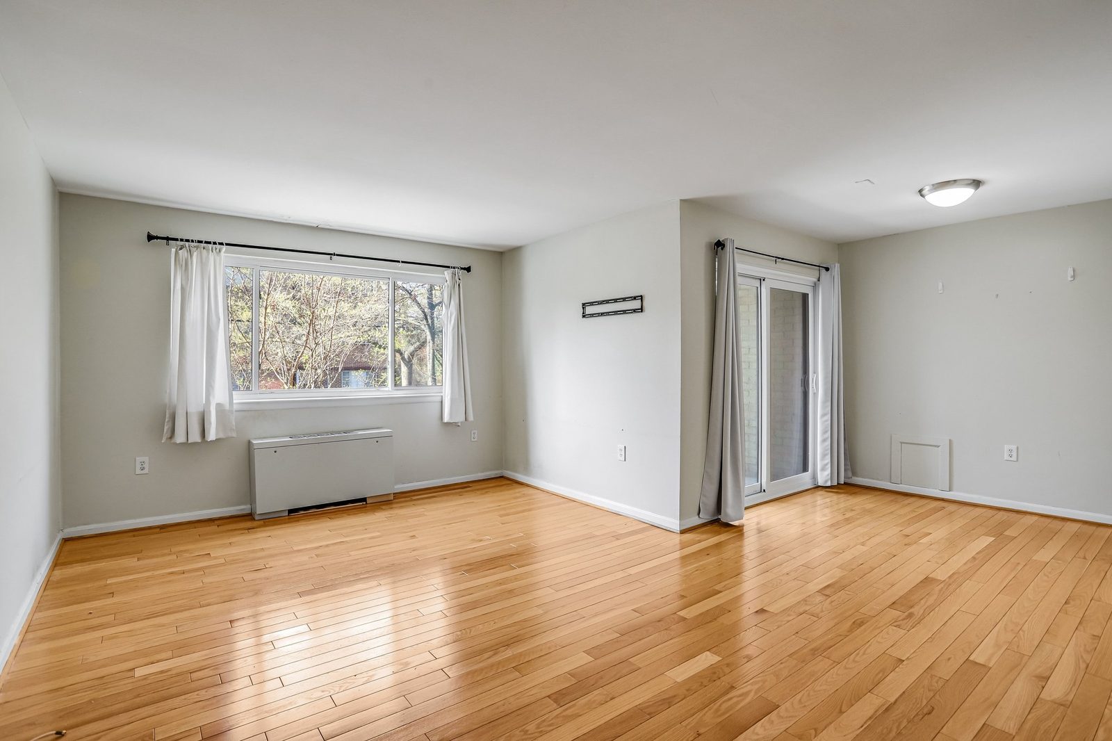 Empty living room with hardwood floors, picture window and sliding glass door