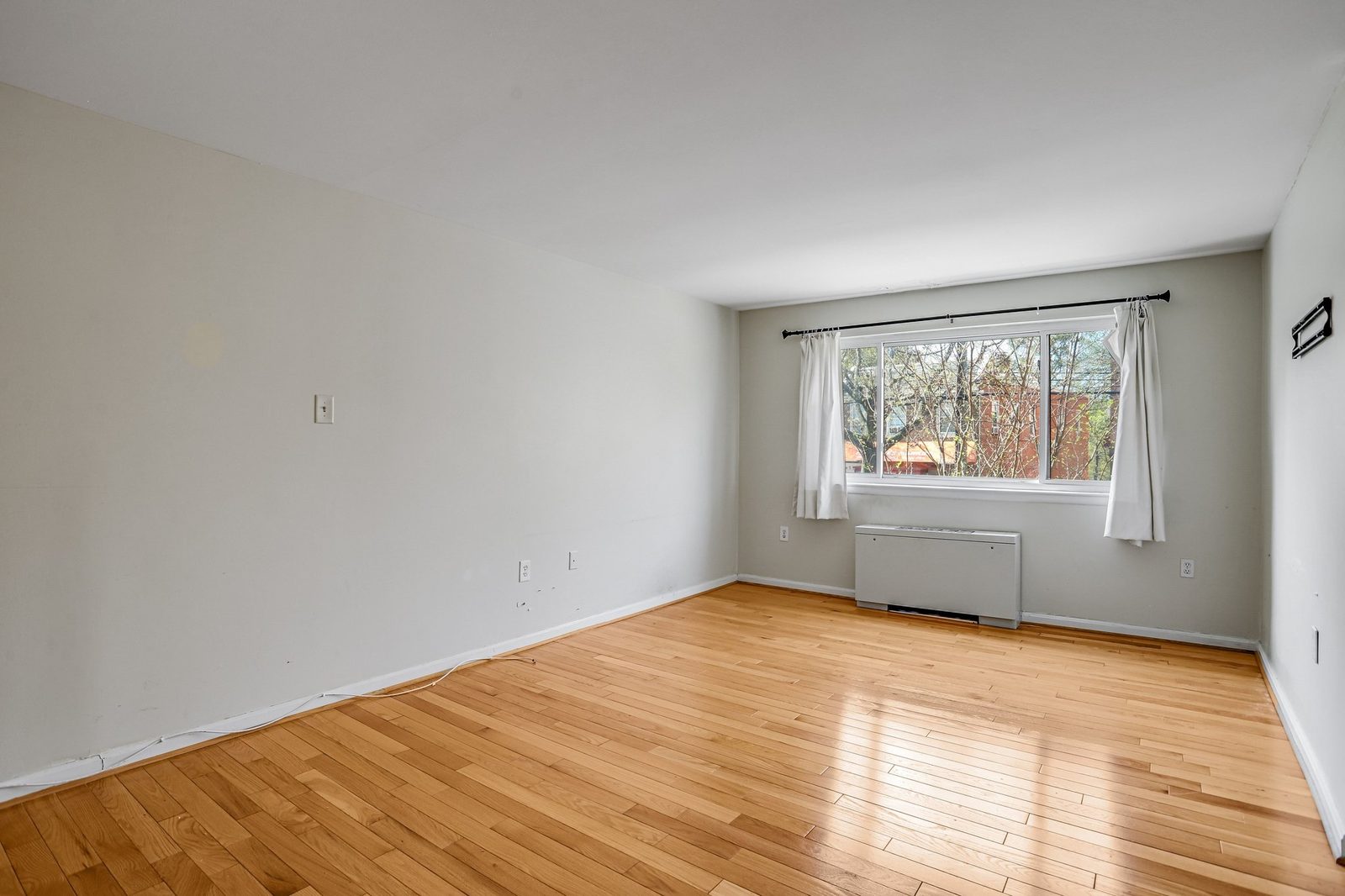 Empty room with hardwood floors, window and through-wall heating unit