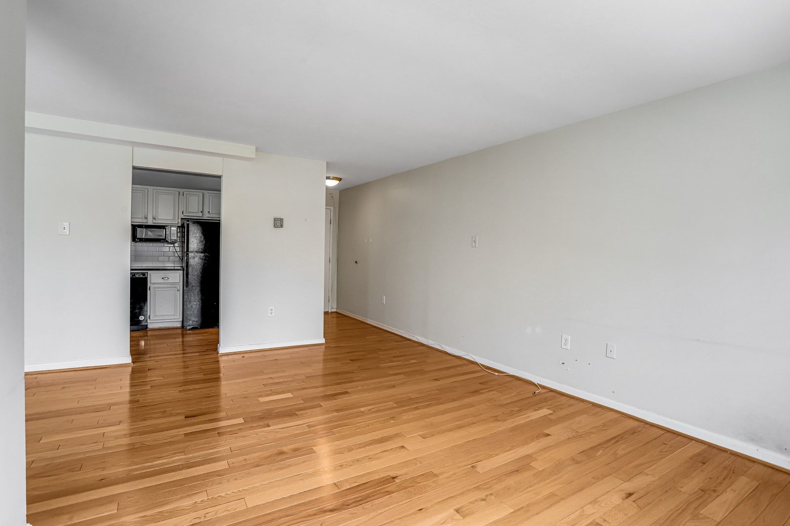 Hardwood-floored room opening to kitchen with black refrigerator and microwave