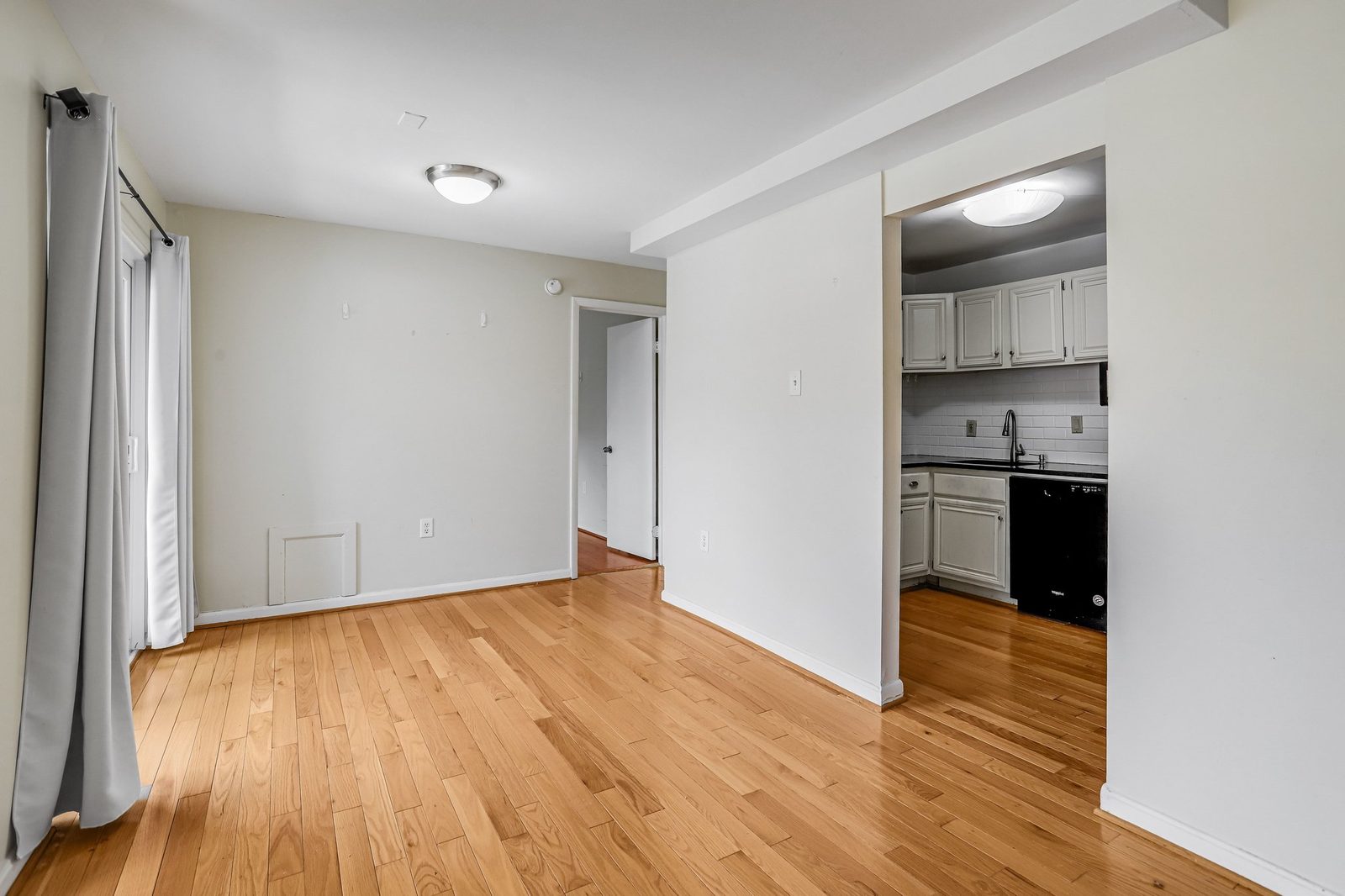 Hardwood floors beside kitchen with white cabinets and subway tile backsplash
