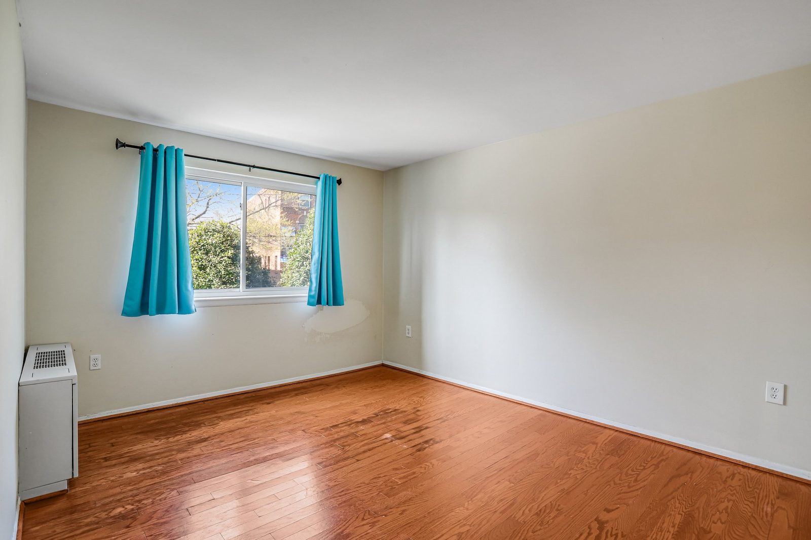 Empty room with oak floors, teal curtains and through-wall heating unit