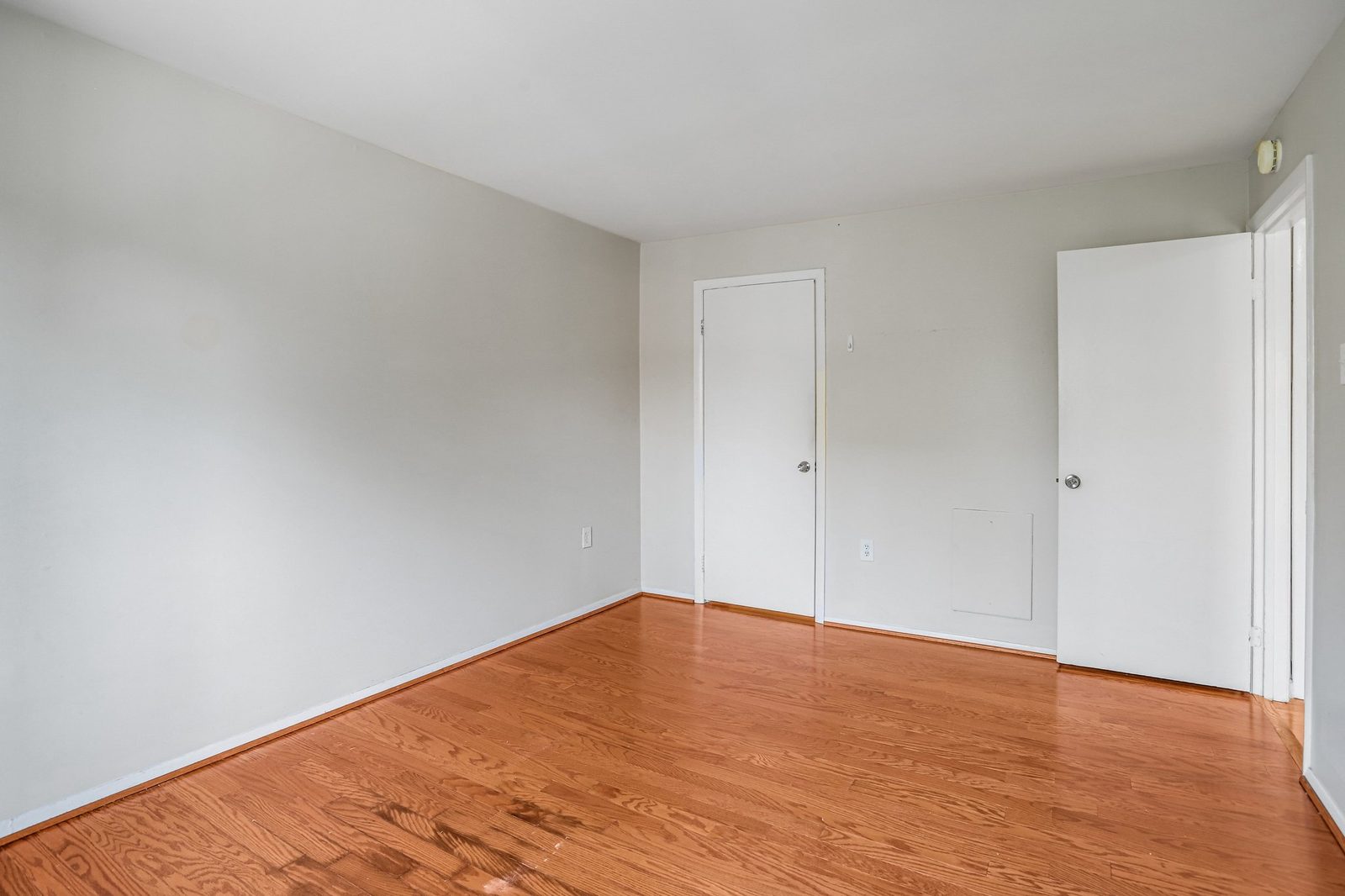 Empty room with oak hardwood floors and two white panel doors