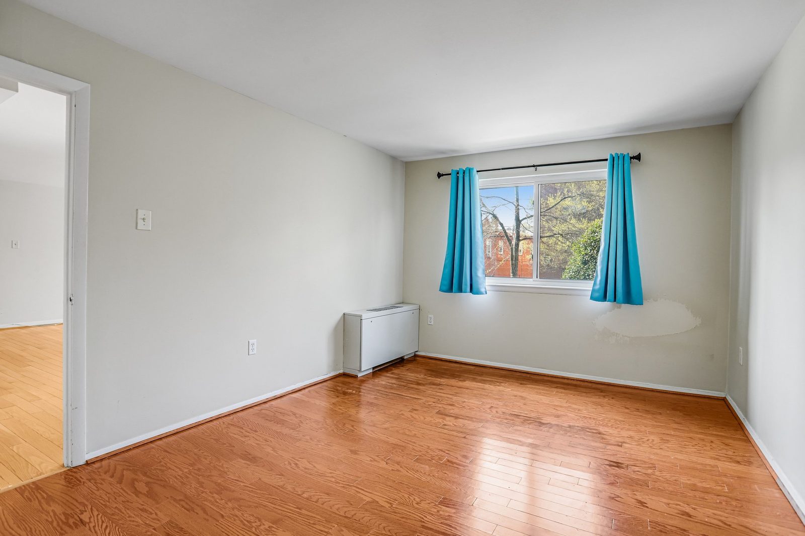 Empty room with oak floors, curtained window and doorway to adjoining room