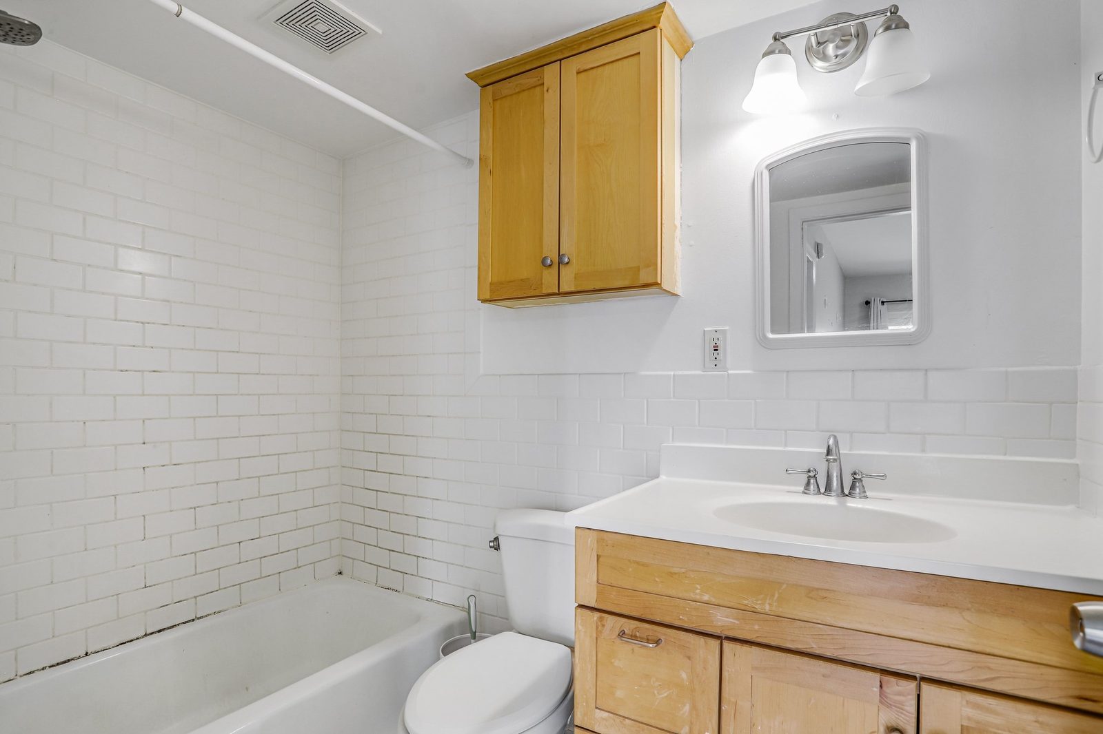 Bathroom with subway-tiled tub surround and light wood vanity
