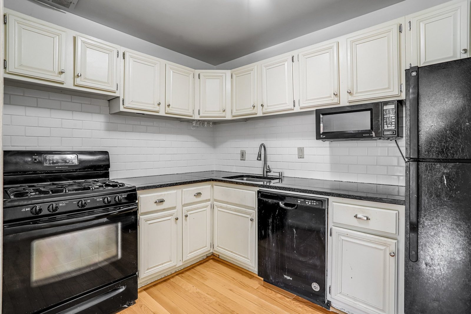 Kitchen with cream cabinets, dark tile counters and black appliances
