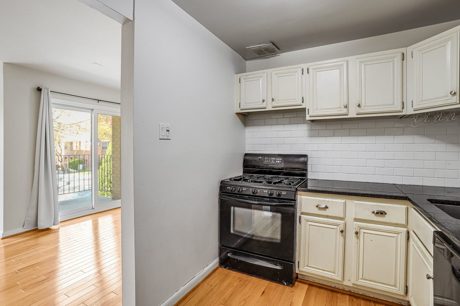 Kitchen opening to hardwood living area with sliding balcony door